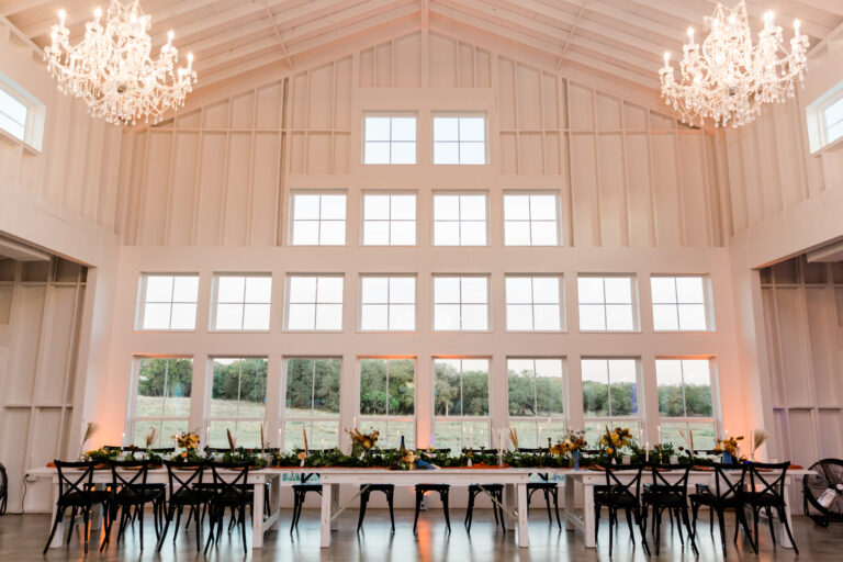 A picturesque outdoor reception space with long banquet tables, decorated with lush greenery and twinkling lights.